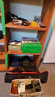 Shelf with camera accessories, boxed Fujinon binoculars, and camera bags.
