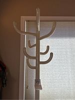 Front view of the upper part of the white metal coat tree showing multiple curved hooks for hanging coats.