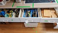 Three open kitchen drawers showing cutlery, utensils and wooden cutting boards.