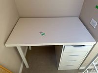 Full view of white laminate desk showing four drawers on the right and two straight supporting legs on the left.