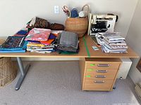 Desk surface shown with fabric stacks, yarn basket, sewing machine, and papers for reference.
