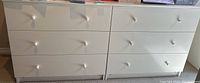 Front view of white laminate dresser with six drawers and round white knobs, showing clean surface and legs.