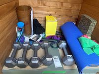 Overview of exercise equipment including six 10 lb hex dumbbells, resistance bands, blue exercise mat, and various small fitness accessories arranged in a corner.