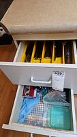 Drawer with knives, forks, and spoons organized in yellow trays, plus additional kitchen items below.