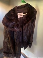Front view of dark brown mink fur coat hanging on a hanger showcasing the design and collar.
