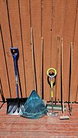 Full view of the six garden tools laid out against a wooden fence showing overall condition and variety