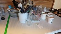 Full lot overview showing measuring cups, utensils, mugs, salad spinner, blender parts on a table against wooden background