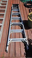 Full length view of aluminum ladder on wooden deck, showing entire ladder with metal braces and rubber foot caps.
