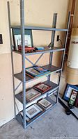 Metal utility shelving unit in a garage, showing five shelves with various items on them (not included). Visible rust spots on metal surfaces.