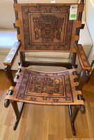 Front view of the rocking chair showing carved leather back and seat on wooden frame.