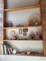 Full view of shelves showing pottery, dolls, artwork plaques, woven baskets and books arranged on three shelves
