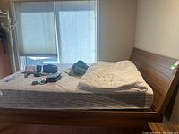 Queen bed with wooden frame, headboard, footboard, and Tempurpedic mattress with white cover folded on top.