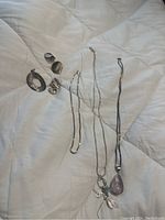 Photo showing all jewellery items including three chains, a pendant, and two sets of earrings laid out on bedding.