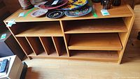 Wide front view of teak wood entertainment storage shelf unit with multiple compartments, shelves, and various plates on top.