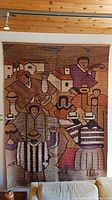 Front view of the large handwoven textile depicting multiple people in traditional Peruvian clothing with village houses in the background.