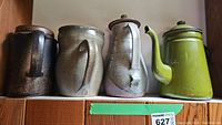 Four pitchers displayed in a row showing different shapes and finishes: three pottery in dark brown, gray, and light pinkish hues, and one green enamelware tea kettle.