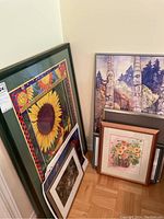 Grouped view of eight framed and unframed art prints in various sizes and themes leaning against a wall on a wooden floor.