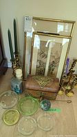 Full lot overview showing framed Asian artwork, brass candle holders, metal box, and glass coasters arranged on floor.