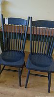Front and slightly angled view of two blue wooden chairs with spindle backs placed side by side.