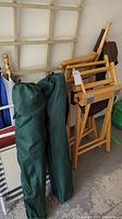 Two wooden director chairs folded up with brown canvas seats and backs, two green bags standing upright beside them