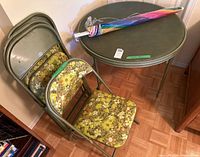 Photo showing vintage round card table with folded chairs and umbrella on top
