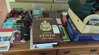 Overall view of the coin album along with other items on the table. The album is brown with gold lettering and crest reading 'Canada Copper Cents 1937-1952'.
