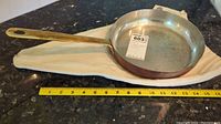 Full view of copper skillet lying on a surface with measuring tape showing length and diameter of skillet.