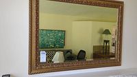 Full view of rectangular mirror with gold carved frame hanging on wall, showing reflection of room.