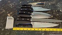 Photo showing six Henkel kitchen knives laid out with measuring tape to show blade length.