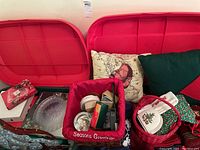 Two red plastic totes filled with assorted holiday cushions, baskets, plates, and decorations with visible red cushions, baskets, and a box.