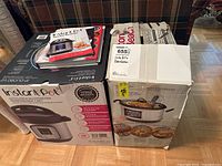 Two boxed kitchen appliances: Instant Pot Duo 7-in-1 programmable pressure cooker and a slow cooker. Manuals and recipe booklets on top of the boxes.