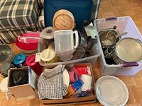 Multiple kitchen items and containers in a cardboard box and plastic bins, various utensils and lids visible