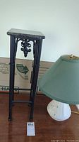 Photo showing the black metal side table with marble top next to the ceramic lamp with green shade on a wooden surface.