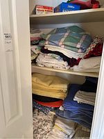Folded assorted linens, towels and bed sheets stacked on shelves in closet area.