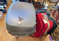 Image showing the large metallic grey hard shell suitcase on the wooden luggage rack with red and black suitcases beside it on the floor.