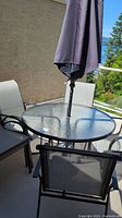 Patio round glass table with umbrella and several patio chairs arranged around it on a balcony.