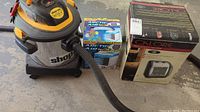 Photo showing the Shop-Vac vacuum, the Calore Pro Utility Heater box, and two Arctic Air evaporative air cooler boxes together on a floor.