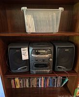 Wide shot showing the stereo system on a wooden shelf with a plastic bin of CDs above and more CDs below on another shelf.