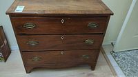 Front view of vintage wooden chest with three drawers and metal oval handles, showing overall wear and aging.