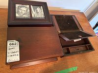 Two vintage wooden boxes, larger with hinged lid and smaller with photo frame on lid, placed on wooden table.