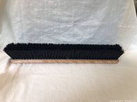 Top side view of the wooden broom brush showing black synthetic bristles densely packed and rectangular shape.