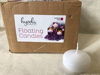 Box of Hyoola Floating Candles with a large white candle displayed in front, showing clean cylindrical white candle with wick.