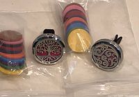 Photo of two metal essential oil car vent clips with decorative fronts and bags of colorful felt scent pads.