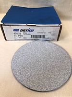 Box labeled Norton Dry Ice with product information and one sanding disc placed in front showing abrasive side.