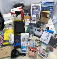 Lot showing a variety of new electronic items including cables, chargers, external storage enclosures, phone cases, adapters, and accessories in retail packaging.