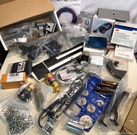 Overview of lot showing many sealed small industrial parts and tools including metal blades, screws, boxed items, and clamps.