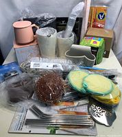 Photo showing assortment of kitchenware items including ceramic pots, metal straws, copper scrubber, and silicone cleaning pads all new and mostly packaged.
