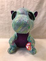 Front view of the 10-inch TY Beanie Boos dragon plush, showing the shiny multicolored scale pattern, large eyes, and purple belly with the TY heart tag attached.