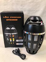 Flame Atmosphere Speaker next to its box showing product name and USB charging cable in front.