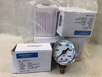 Photo of multiple Ashcroft pressure gauges in original boxes showing product with clear labeling.